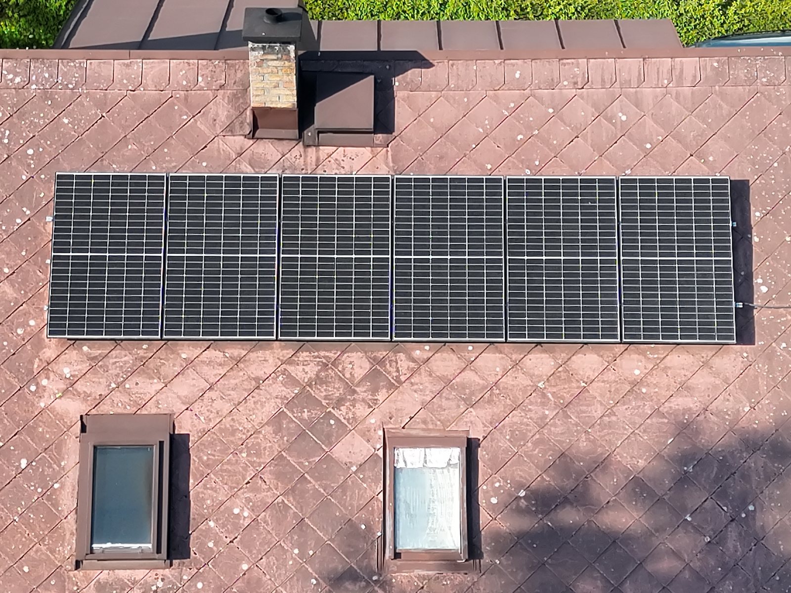 Kolmý dronový snímek střechy s fotovoltaickými panely, komínem a střešními okny