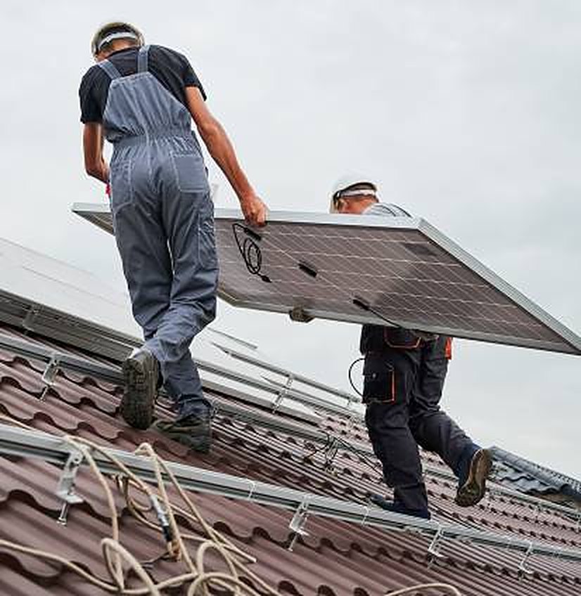 Montážníci vynášejí fotovoltaický panel na střechu
